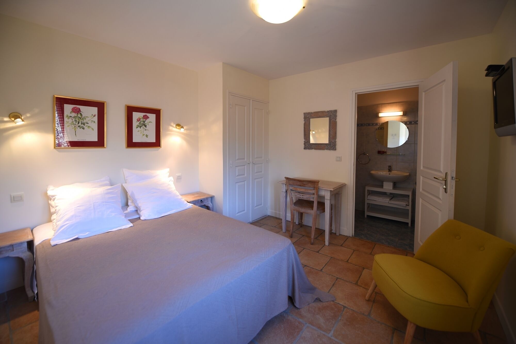 Un dormitorio con cama, mesitas de noche, escritorio, silla y baño visible a través de una puerta abierta.