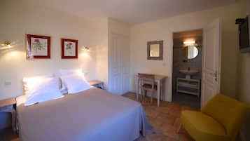 Un dormitorio con cama, mesitas de noche, escritorio, silla y baño visible a través de una puerta abierta.