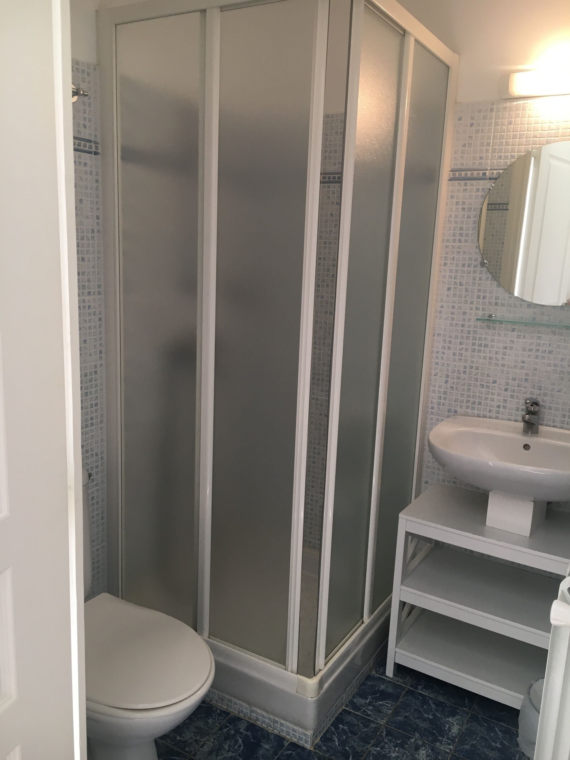 Un baño con ducha de vidrio, inodoro blanco y lavamanos blanco con espejo sobre él.