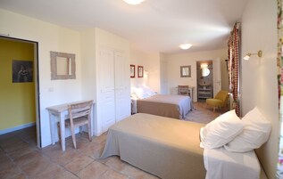 Un dormitorio con dos camas, un escritorio y una silla. Se ve un baño al fondo.