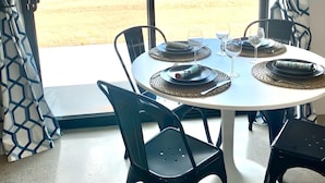 Uma sala de jantar com uma mesa posta para dois, cadeiras e vista para uma paisagem desértica através de grandes janelas.