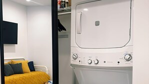 Quarto compacto com cama, máquina de lavar e pequena cozinha.