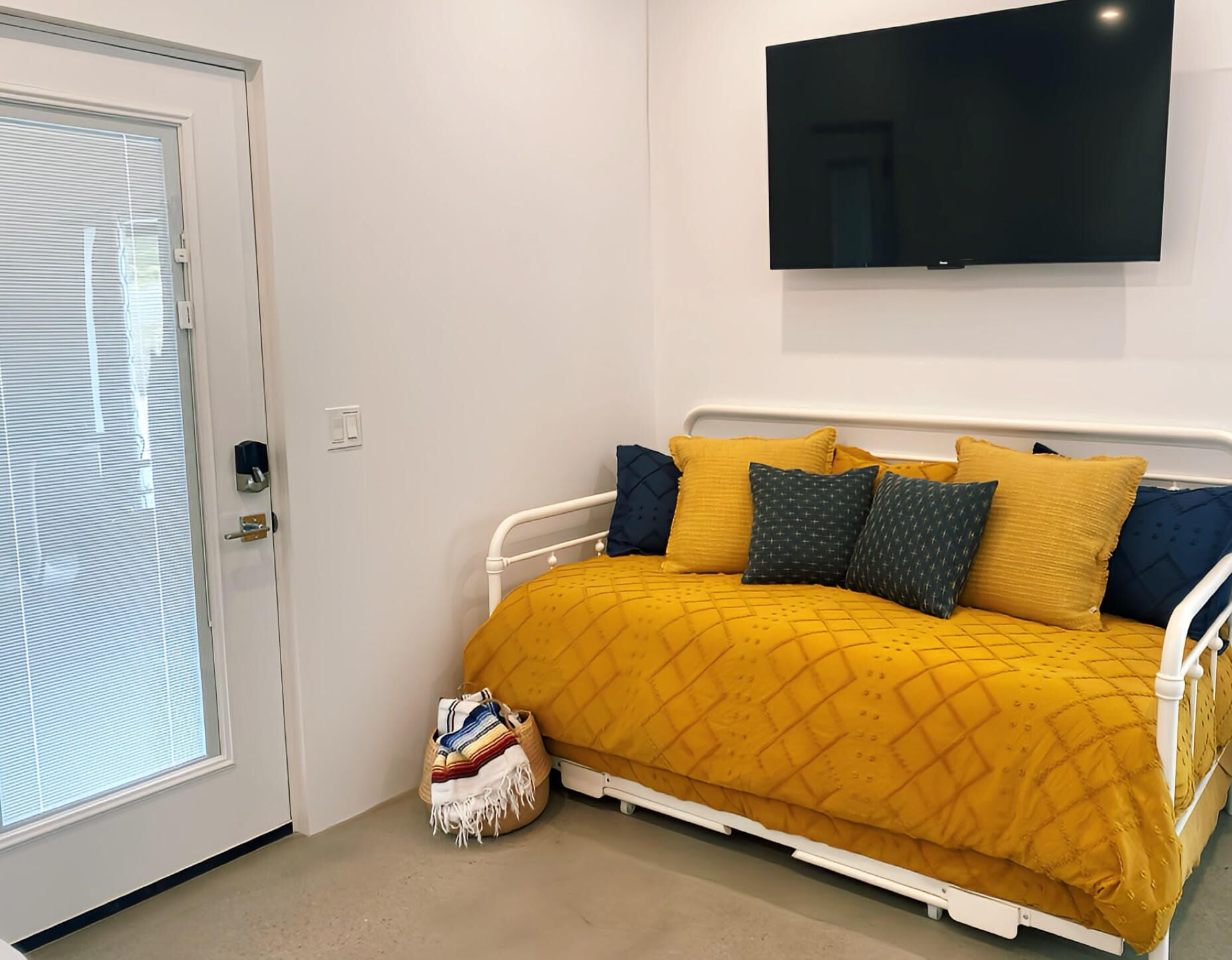 Un dormitori amb llit, televisió penjada a la paret i una porta amb finestreta.