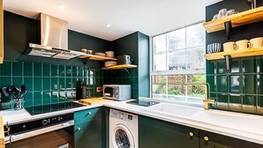 A modern kitchen with a dishwasher, washing machine, and a window with a view of greenery.