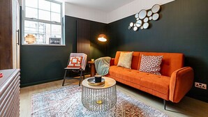 A modern living room with a dark wall, an orange sofa, a patterned rug, and a round coffee table.