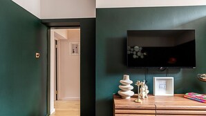 A modern living room with a dark green wall, a flat-screen TV mounted above a wooden console, and a door leading to another room.