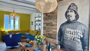 A dining area with a wooden table set for two, a large painting on the wall, and a yellow sofa in the background. - Villa Ker Tesson: Private Jacuzzi, Port 700m, Fisherman's House, 10 guests (L'Île-d'Yeu)