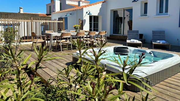 A wooden deck with a hot tub, outdoor seating, and a white building with windows and a tiled roof. - Villa Ker Tesson: Private Jacuzzi, Port 700m, Fisherman's House, 10 guests (L'Île-d'Yeu)