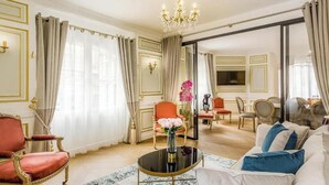 A luxurious living room with a chandelier, red and white furniture, and a large window with curtains.
