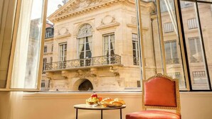 A room with a view of a historic building, a table with food, and a red chair.