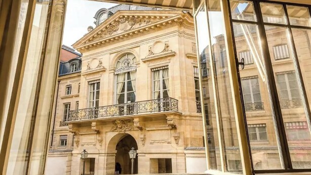 A historic building with classical architecture, featuring a central entrance, ornate balcony, and large windows.