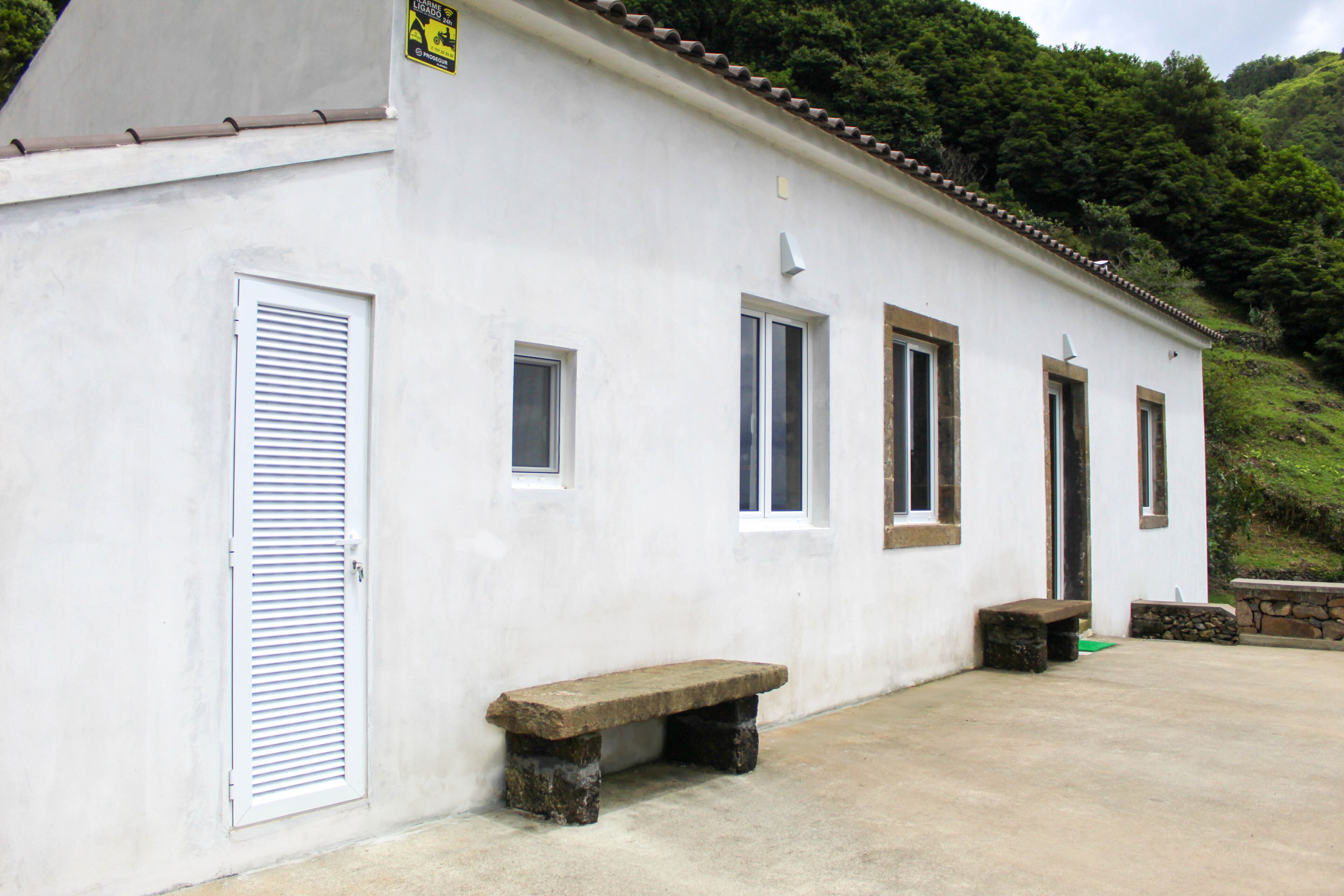 A white building with a sloped roof, a bench, and a door with shutters.
