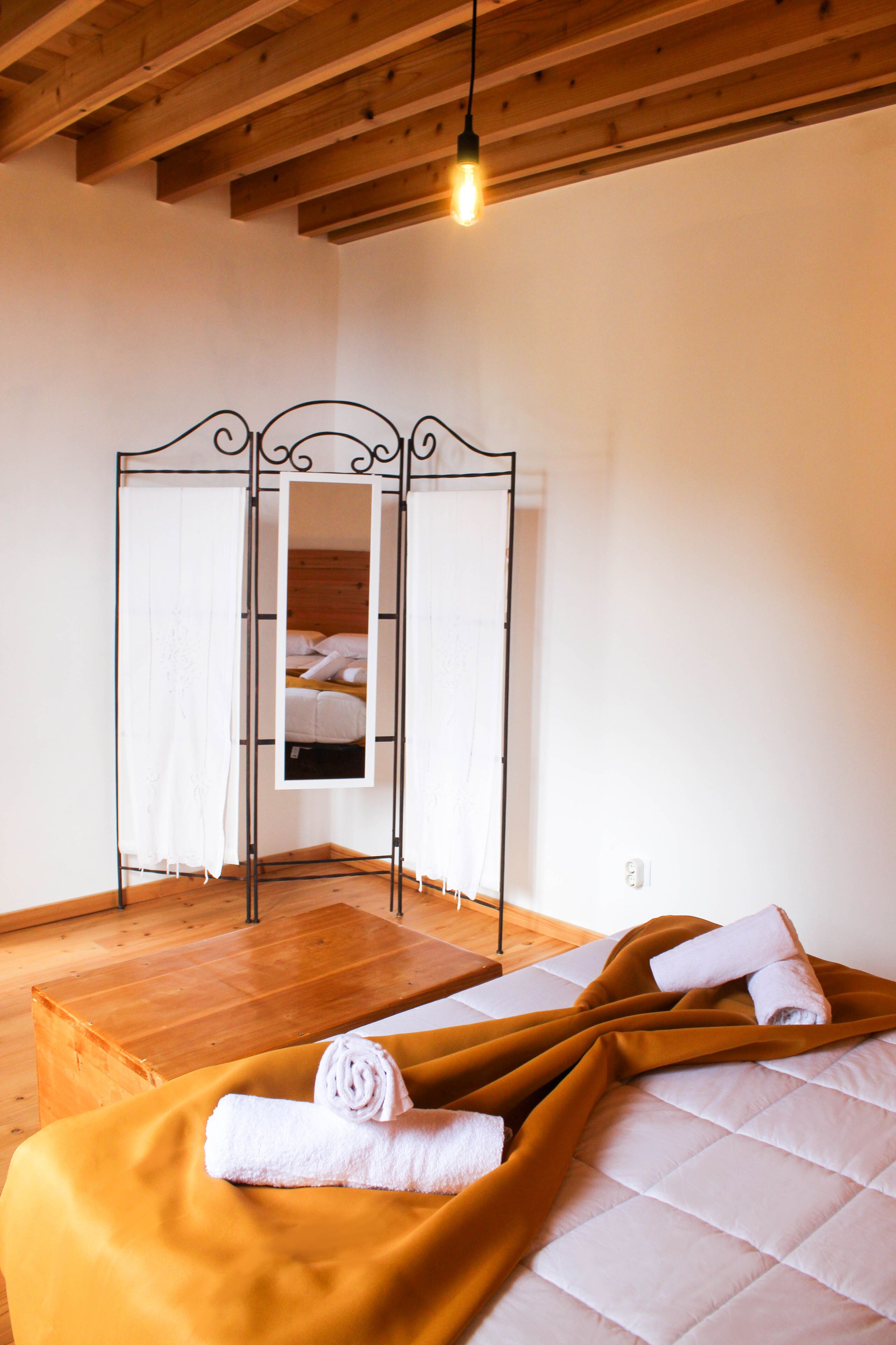 Un dormitorio con techo de madera, cama con edredón blanco, manta marrón y estructura de cama de metal.