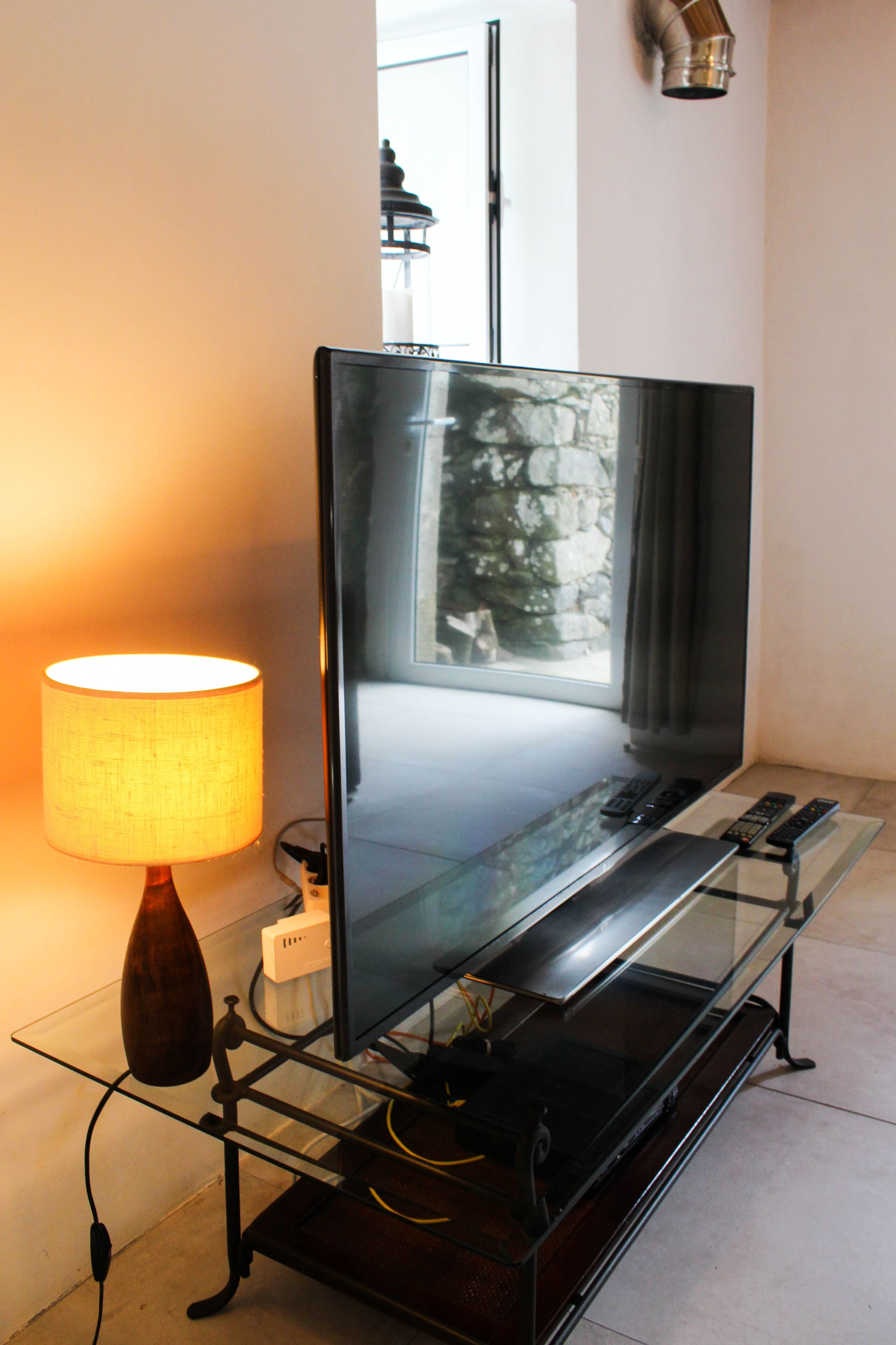 A flat-screen TV on a glass TV stand with a lamp beside it.