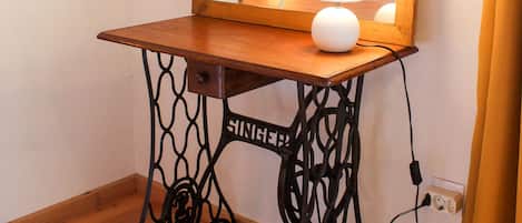 A wooden vanity table with a mirror, a lamp, and a power outlet.
