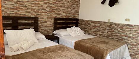Habitación de hotel con dos camas, cada una con cubrecama marrón y ropa de cama blanca. Se aprecia una pared con diseño de ladrillo y un aplique de pared.