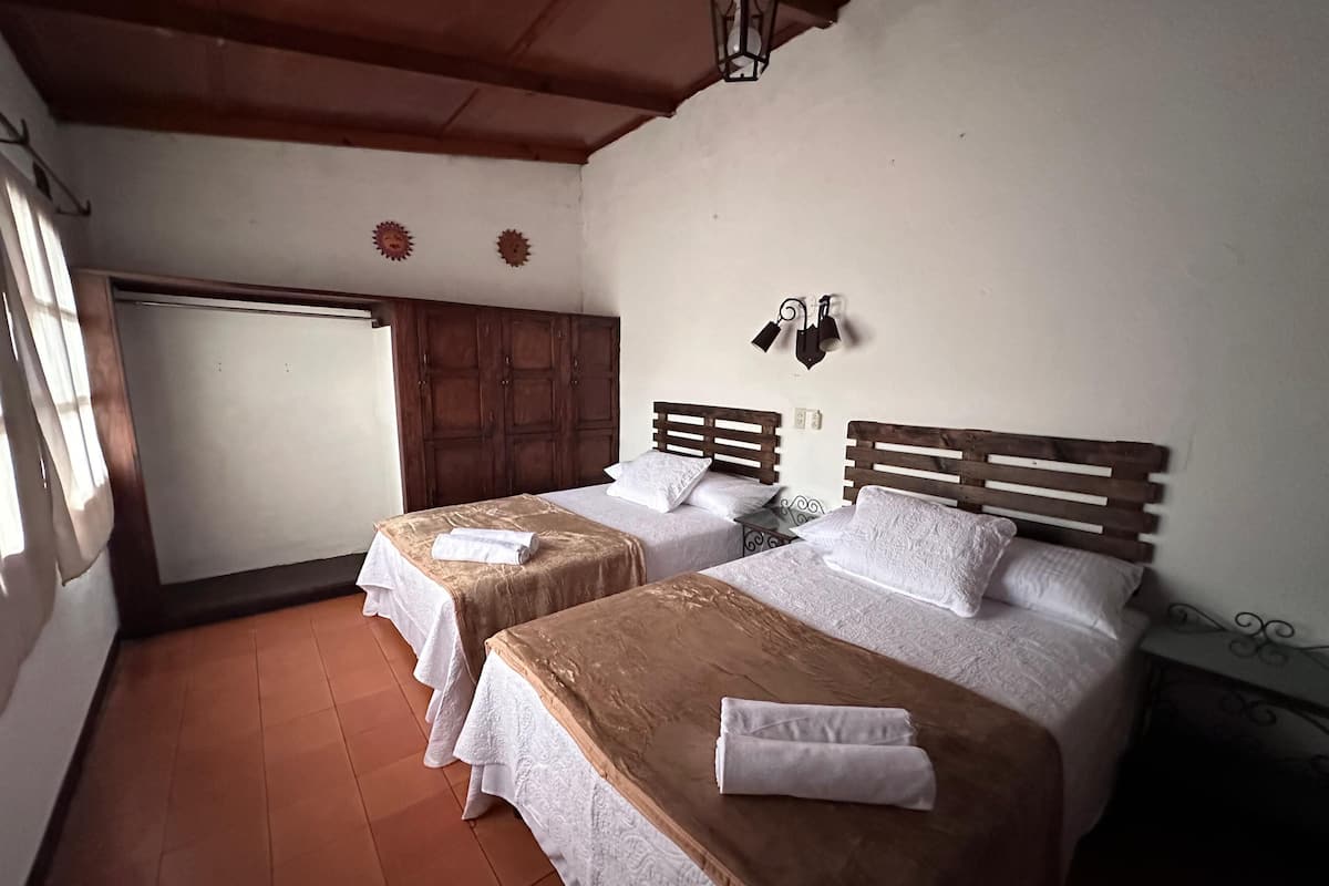 A room with two beds, wooden headboards, a large wardrobe, and a small table.