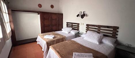 A room with two beds, wooden headboards, a large wardrobe, and a small table.