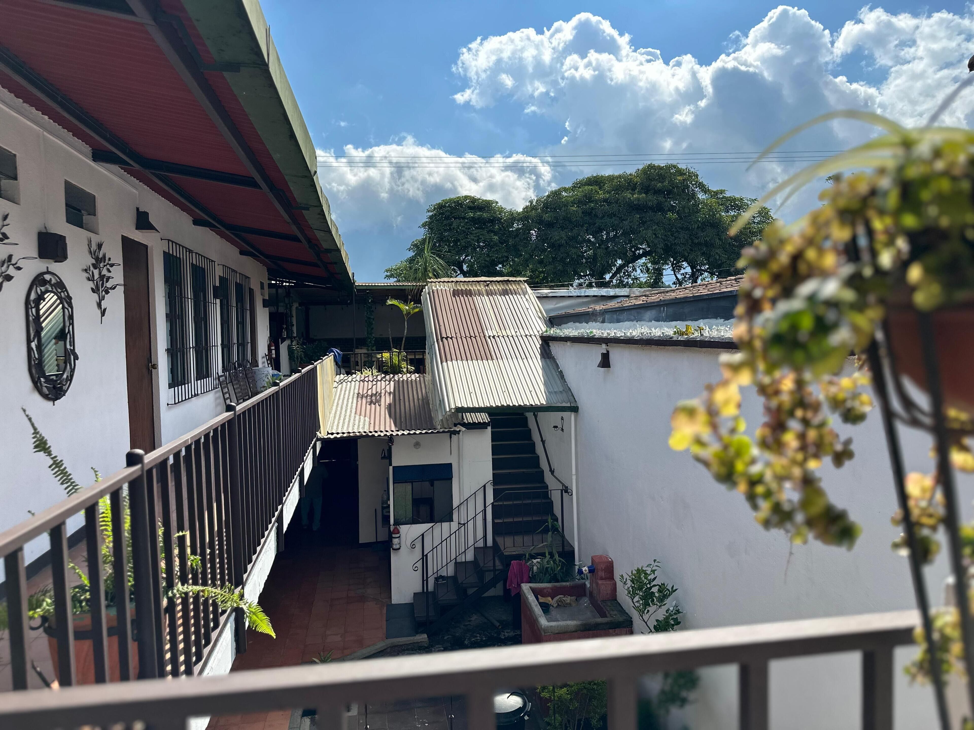 Un edificio residenziale con una scala che porta a un secondo piano, un balcone con tetto in lamiera ondulata e vista sul cielo e sulle nuvole.