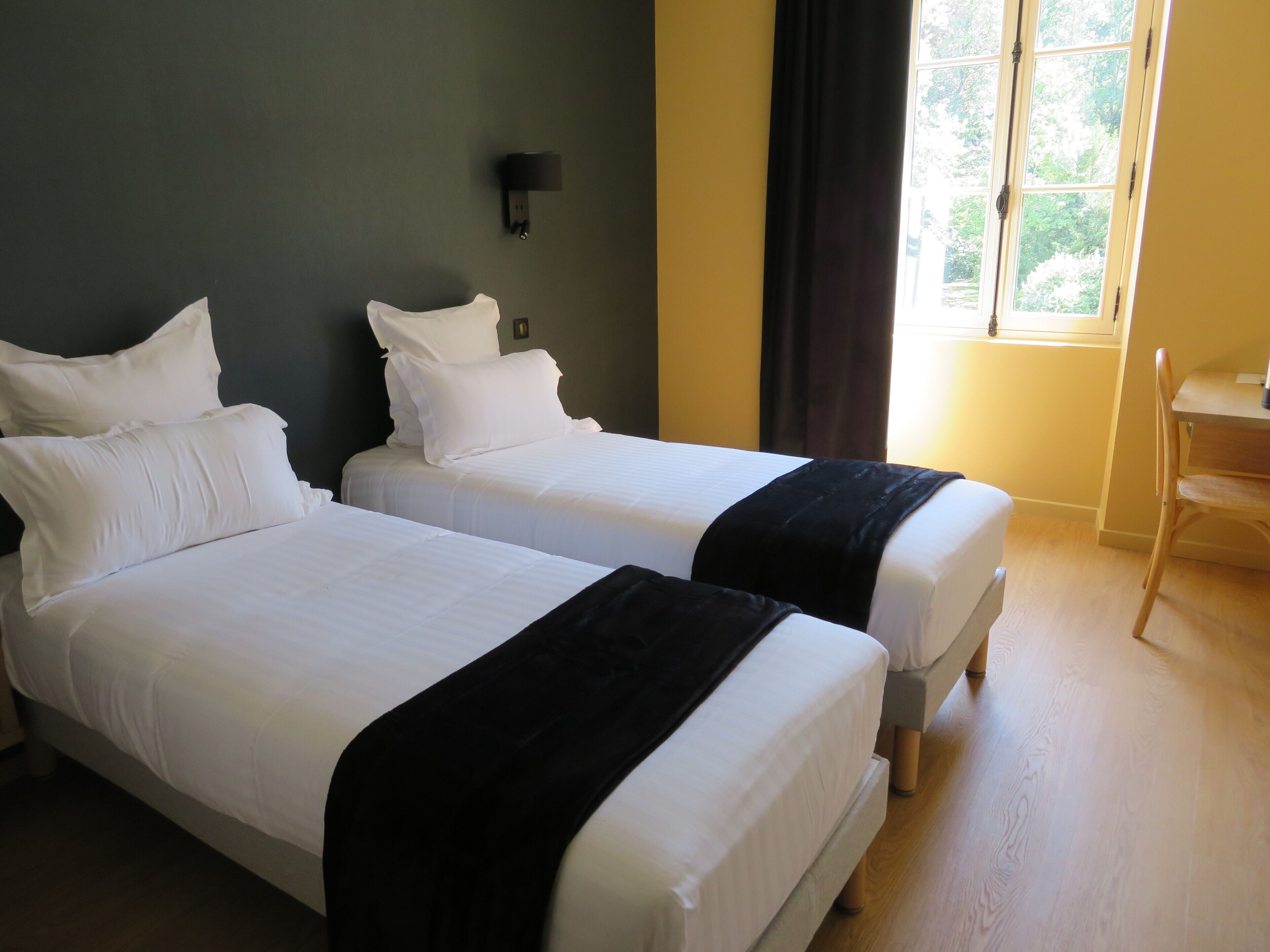 A hotel room with two beds, a small table, and a window with curtains.