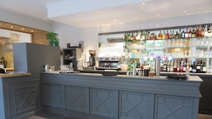 A bar area with a counter, shelves of bottles, glasses, and a coffee machine. - Le Relais de Montignac (Montignac)