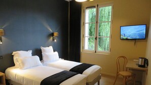 A hotel room with two beds, a TV, a desk with a coffee maker, and a window with a view of greenery. - Le Relais de Montignac (Montignac)