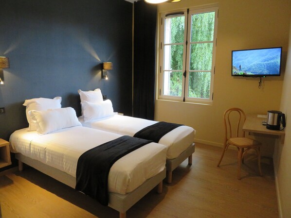 Une chambre d’hôtel avec deux lits, une télévision, un bureau avec une machine à café et une fenêtre donnant sur un paysage verdoyant.