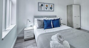 Un dormitorio moderno con cama, mesitas de noche, armario y una obra de arte en la pared.
