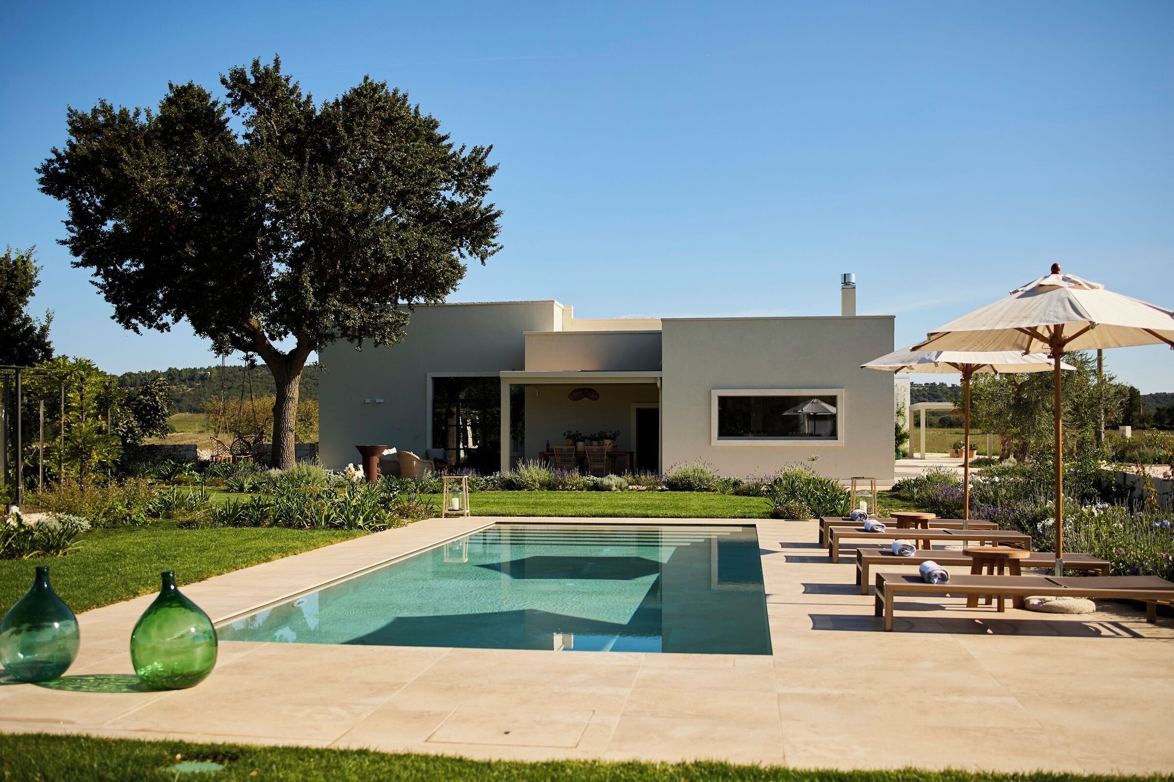 Una casa moderna con piscina, mobiliario de exterior y un gran árbol.