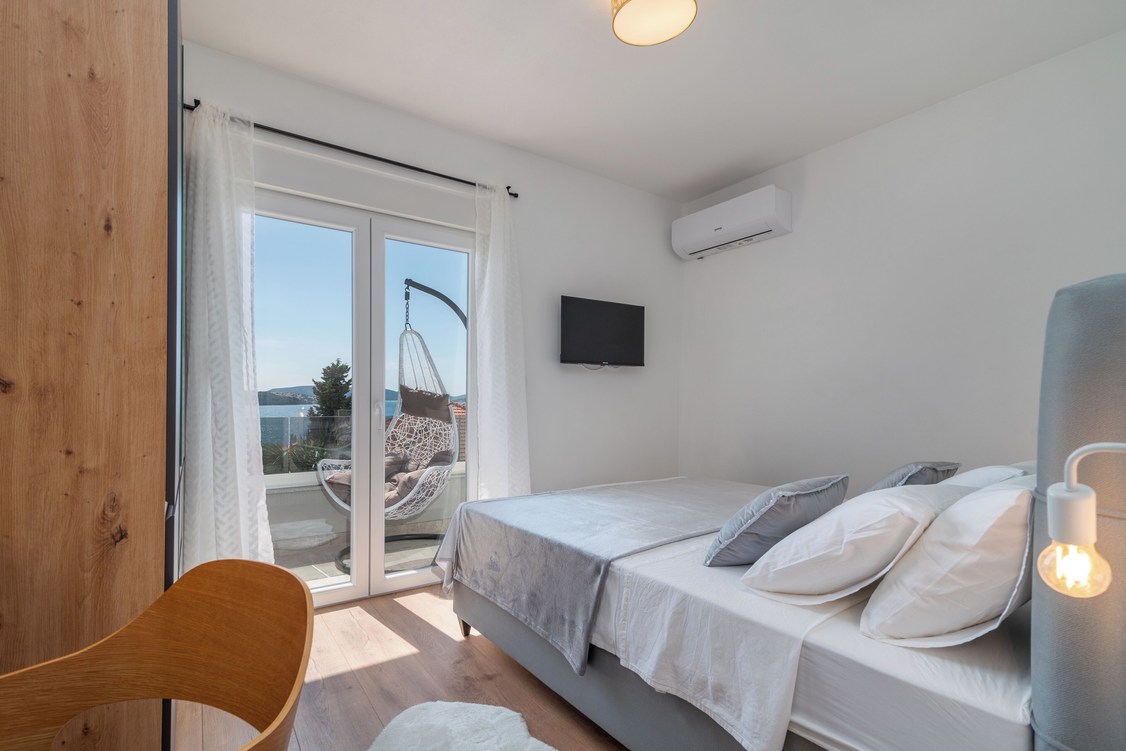 A bedroom with a bed, a chair, a television, and a view of the outdoors.