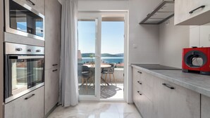 A modern kitchen with a sliding glass door leading to a balcony with a view of the sea. - Villa Eight by D (Okrug)