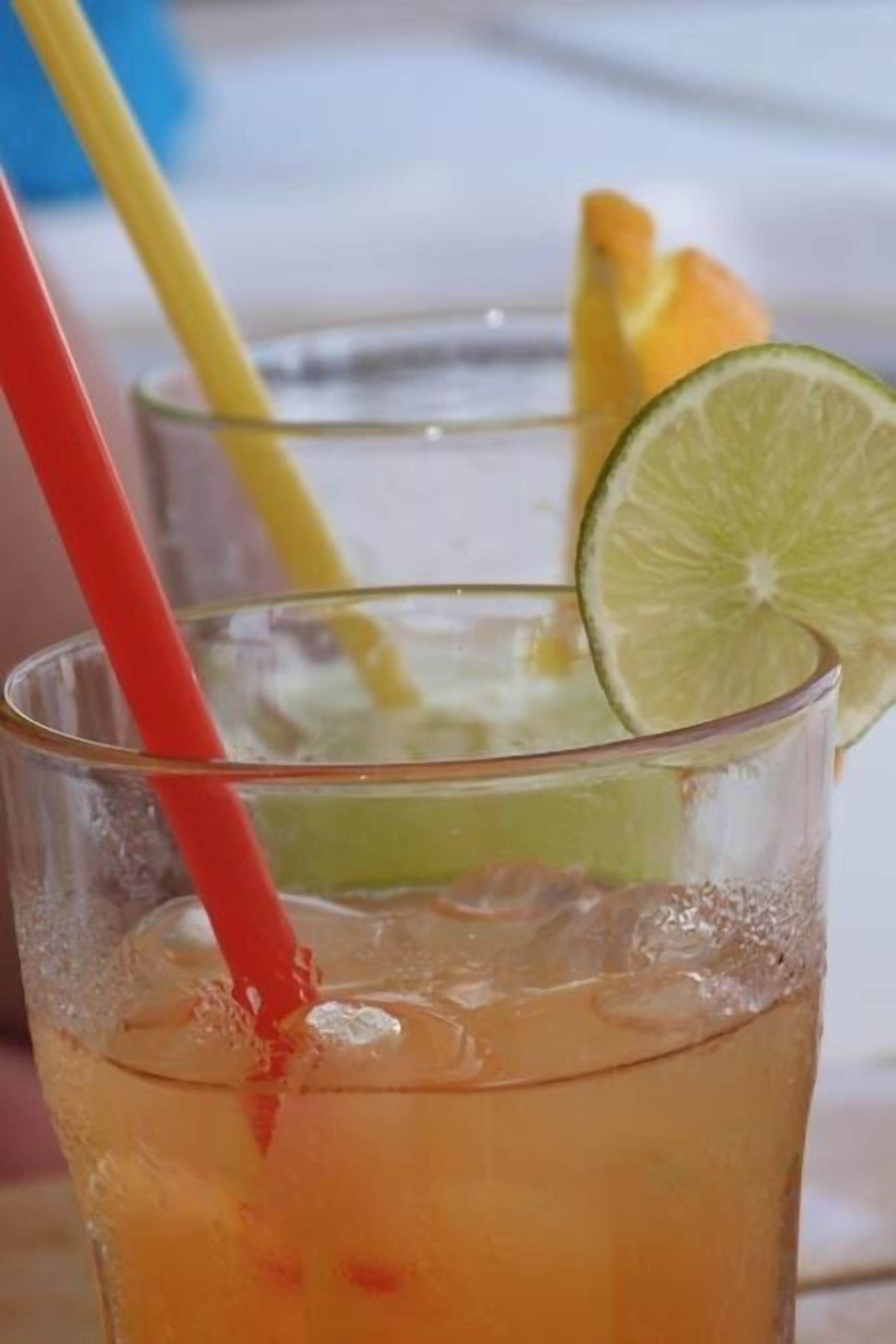 Un bicchiere di bevanda fredda con una fetta di lime e una cannuccia rossa.