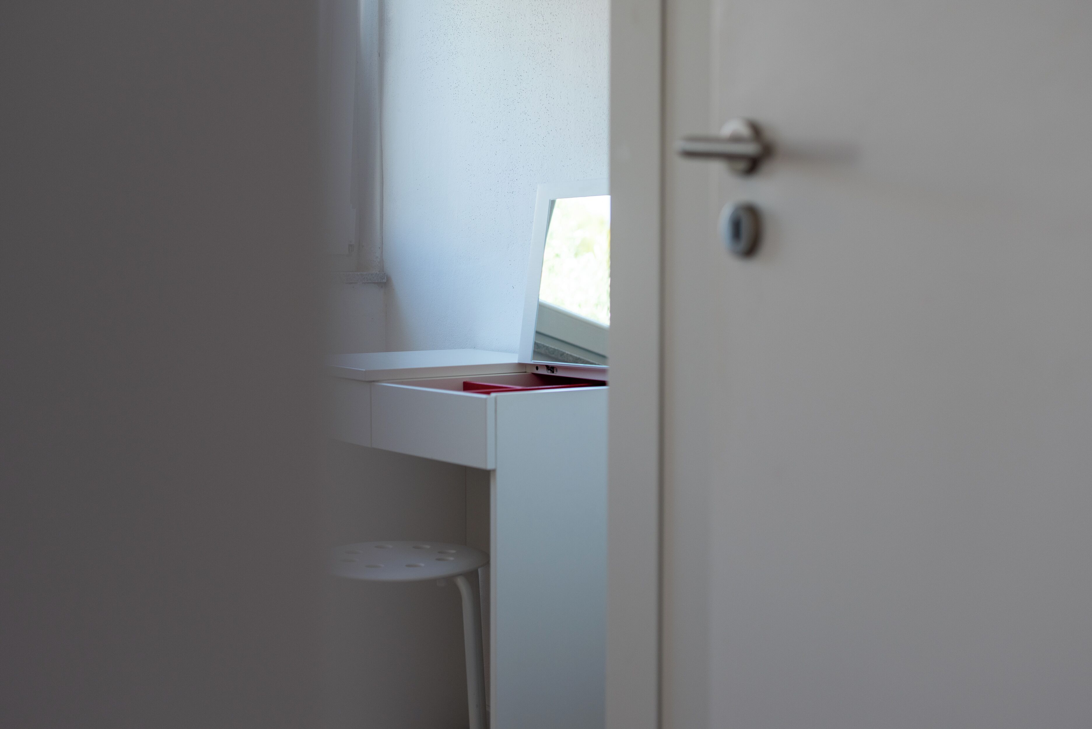 A white door with a handle, a small white shelf with a red object, and a white wall.