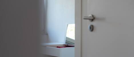 A white door with a handle, a small white shelf with a red object, and a white wall.