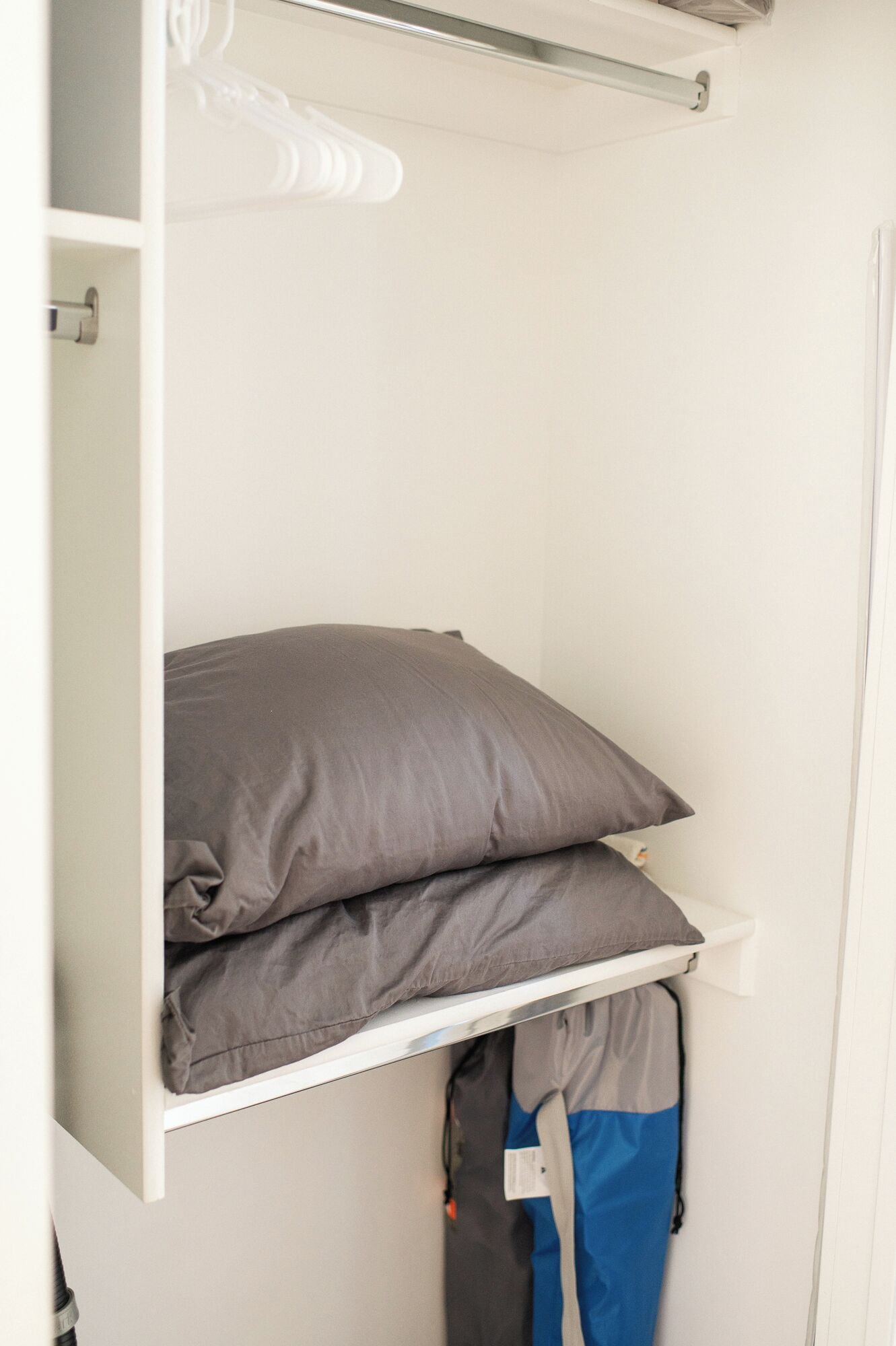 A closet with shelves holding pillows and a bag.