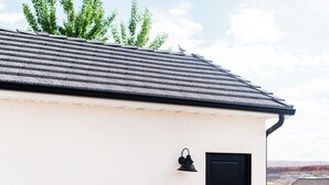 Une terrasse sur le toit, aménagée avec des meubles en osier, une table noire et un luminaire noir fixé au mur.