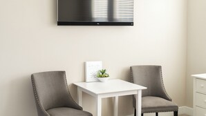 Une pièce moderne avec deux fauteuils gris à revêtement en tissu, une table blanche et un téléviseur à écran plat fixé au mur.