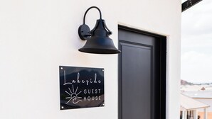 Une porte noire avec une enseigne indiquant « LakeSide Guest House » et un luminaire noir fixé au mur.