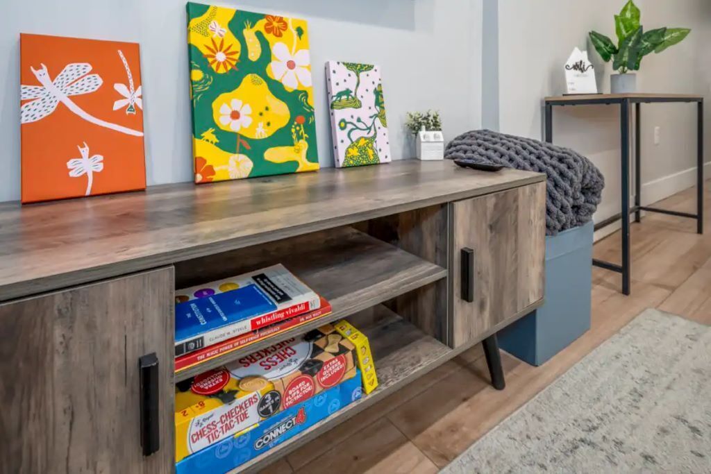 A wooden console table with three colorful paintings, a chess set, and a small potted plant.