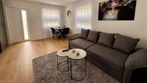 A living room with a grey sofa, a small round table, and a dining area with a table and chairs. - Park View Studio - Features Free Wifi, Bright Furnishings and Modern Facilities (Nijmegen)