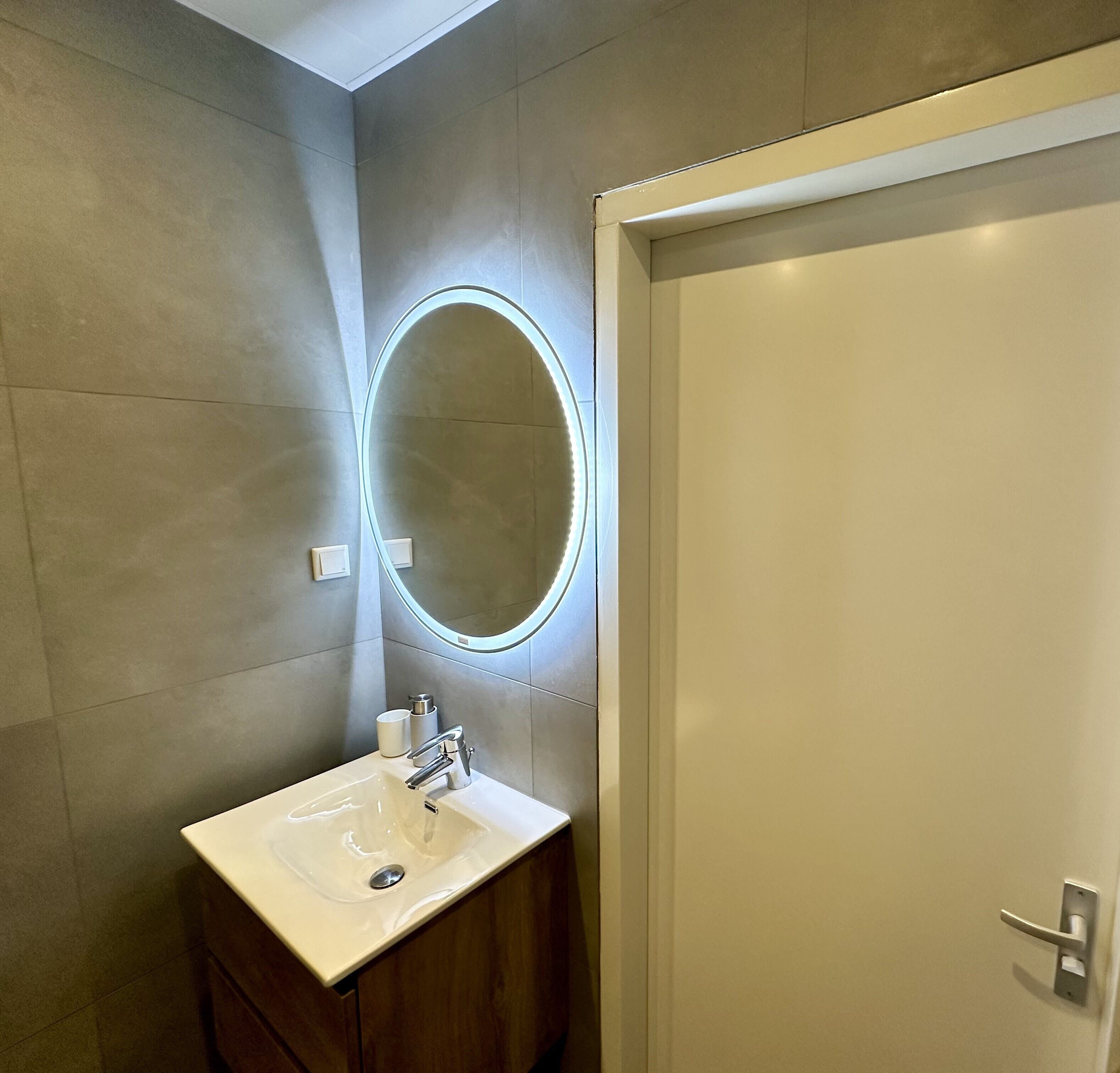 A bathroom with a white sink, a mirror with a light, and a door.
