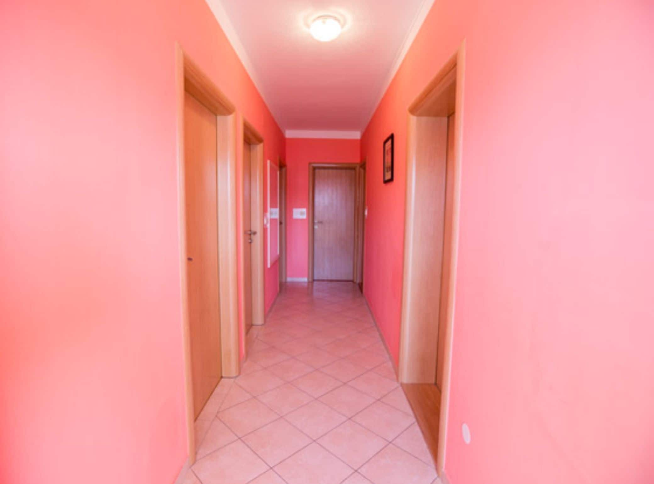 A corridor with pink walls and a tiled floor, leading to a door at the end.