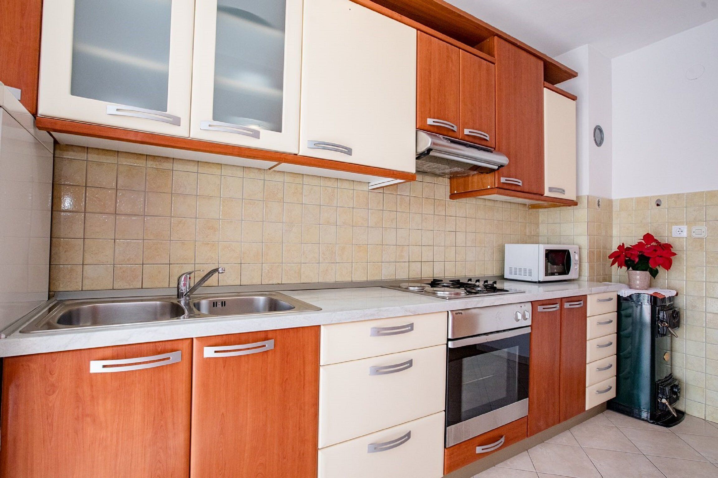 Una cocina con armarios de madera, un lavamanos de acero inoxidable, un microondas y un horno.