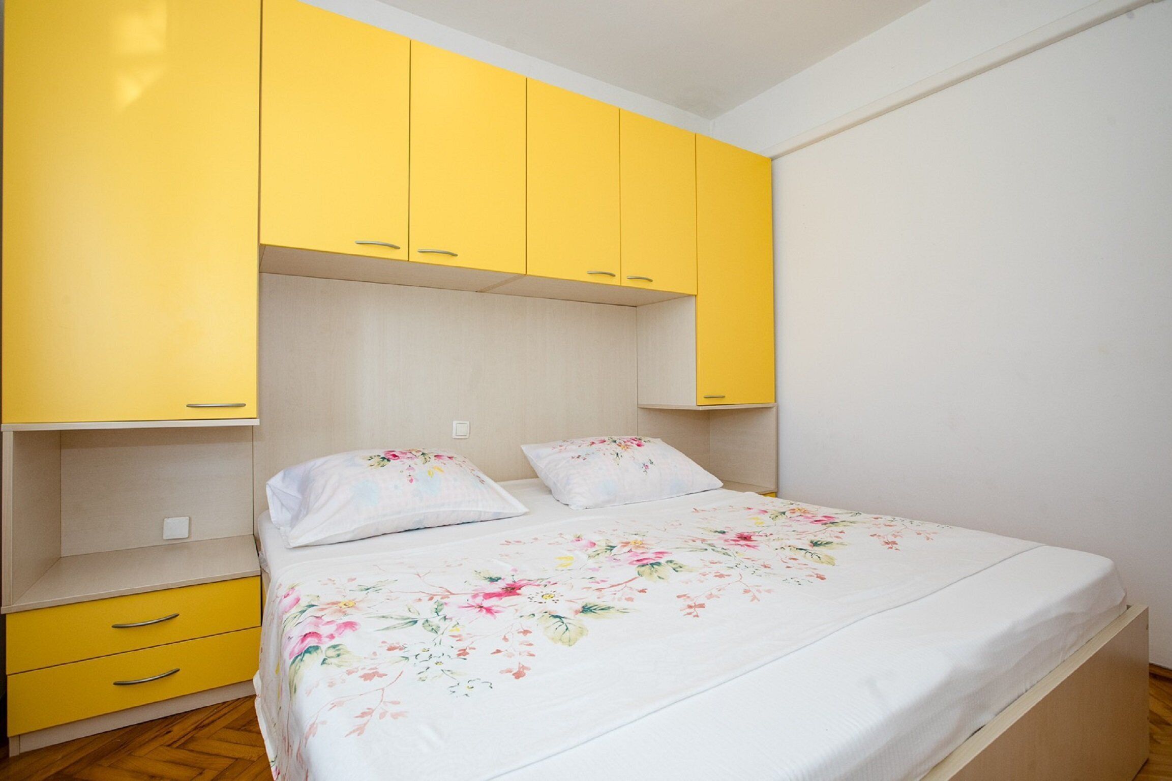 Un dormitorio con una cama, dos almohadas, una mesita de noche y armarios amarillos.