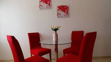 A dining area with a round glass table, four red chairs, and two floral wall art pieces.