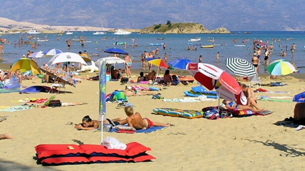 Une plage bondée où les gens se prélassent au soleil et se baignent, avec des parasols et des chaises de plage.