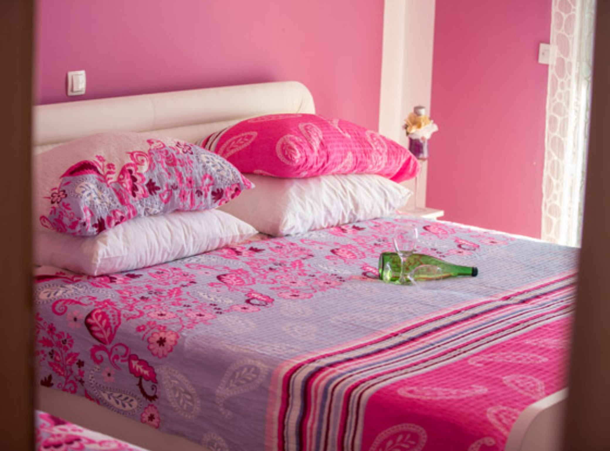 Un lit avec une literie rose, un verre d’eau et un objet décoratif sur la table de chevet.