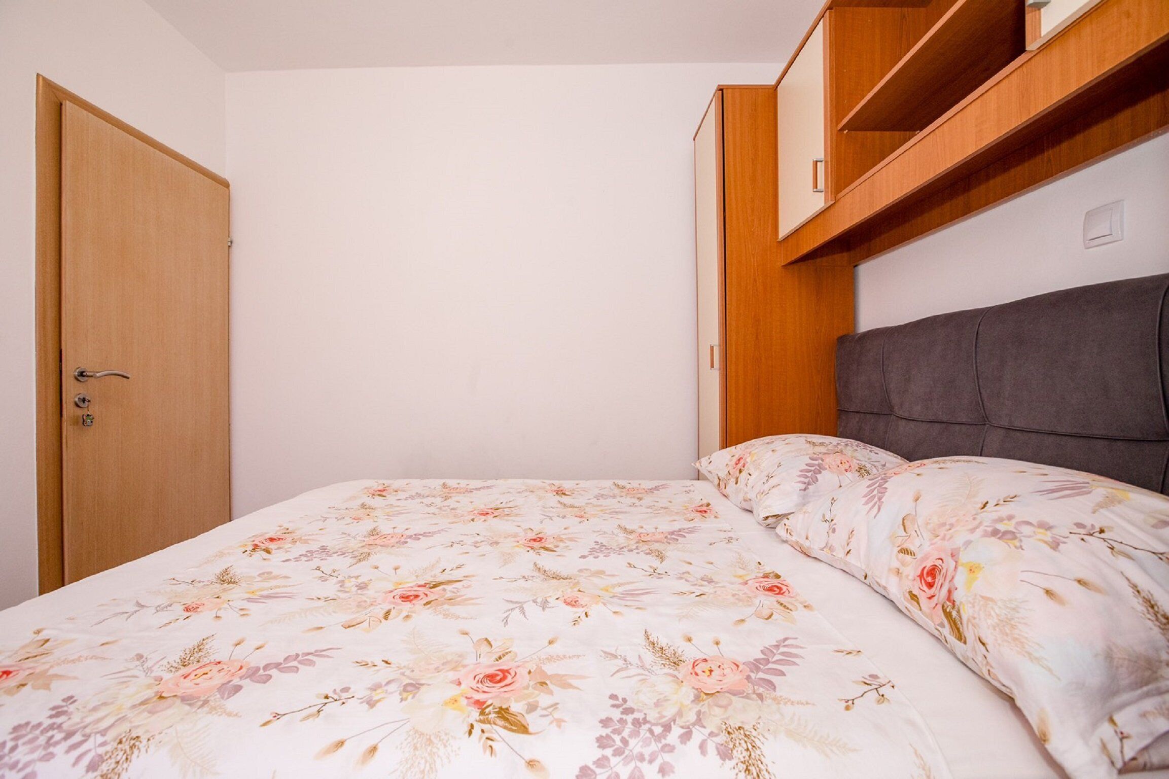 Une chambre à coucher avec une couvre-lit à motifs floraux, une armoire en bois et une tête de lit intégrée.