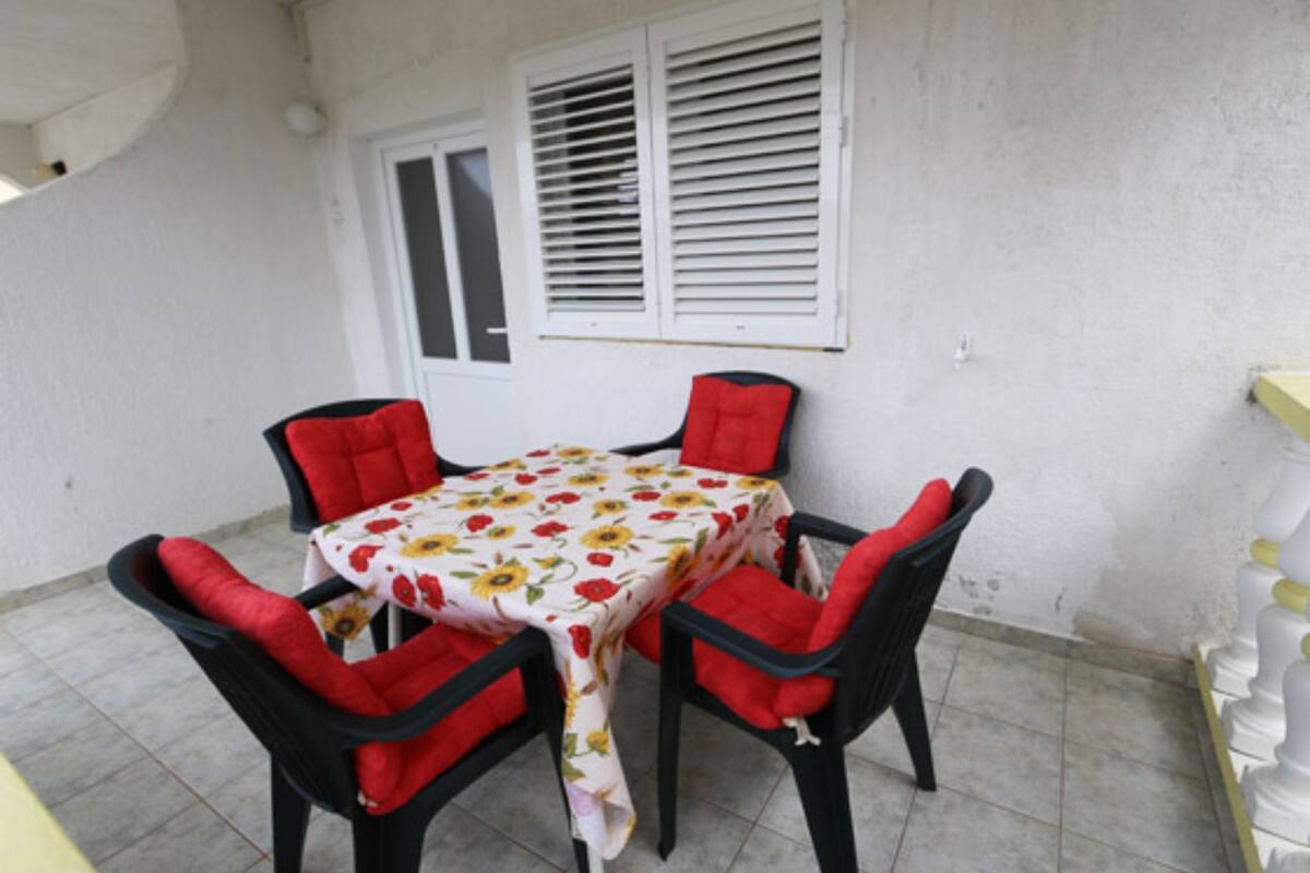A small outdoor dining area with a table and four chairs, each with red cushions.
