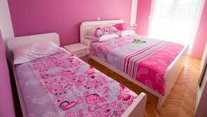 Une chambre avec deux lits, des murs roses et une fenêtre ornée de rideaux légers.